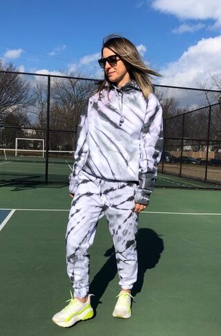 Woman wearing DIY tie dye matching sweatsuit in sunglasses and sneakers on tennis court