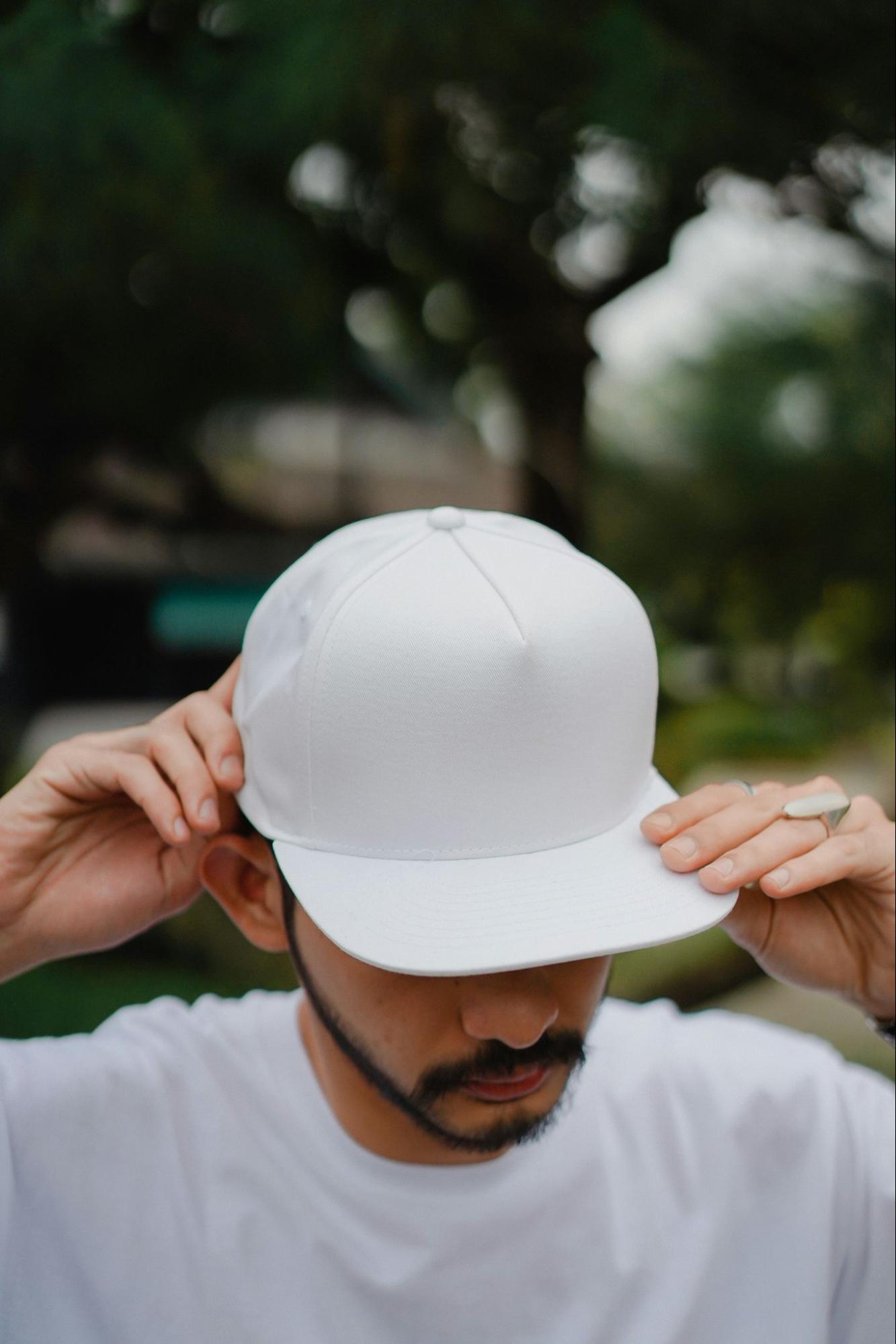 A man wearing a white fitted hat adjusts the brim with both hands.